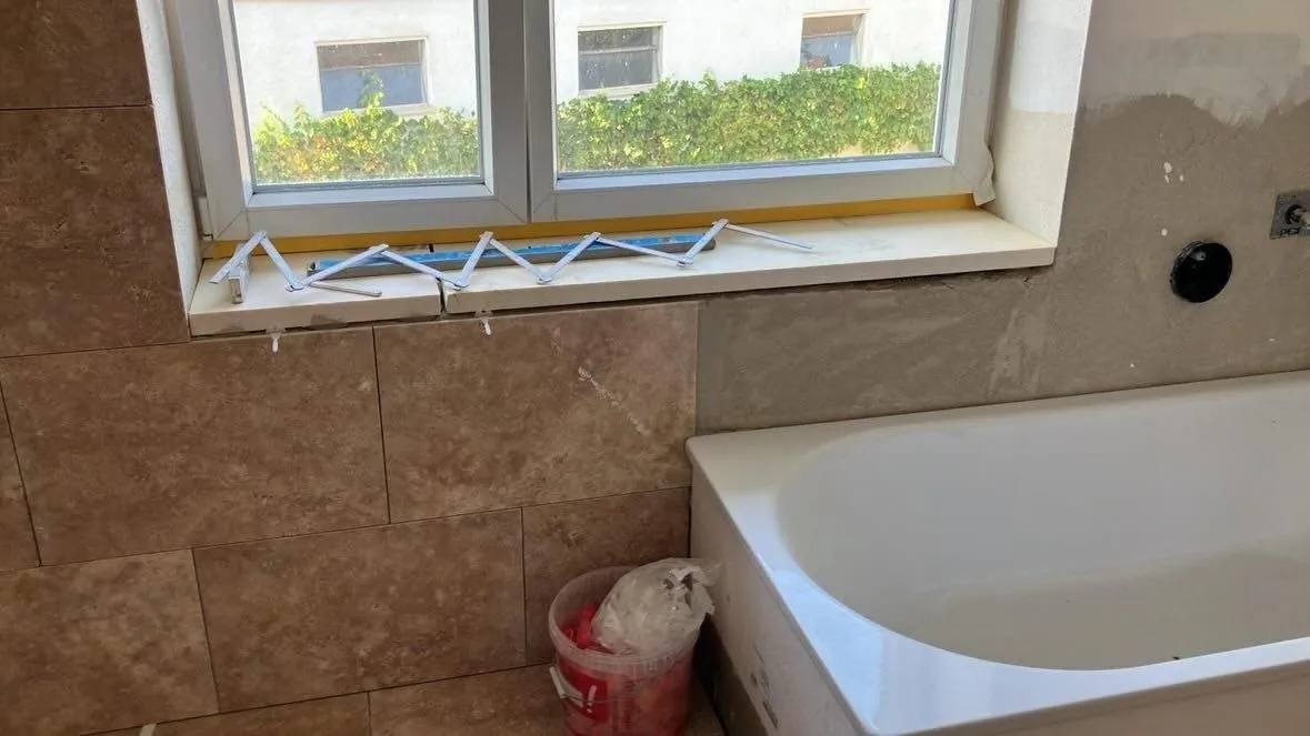 Badewanne unter dem Fenster, eingefasst mit Naturstein in Travertin-Optik