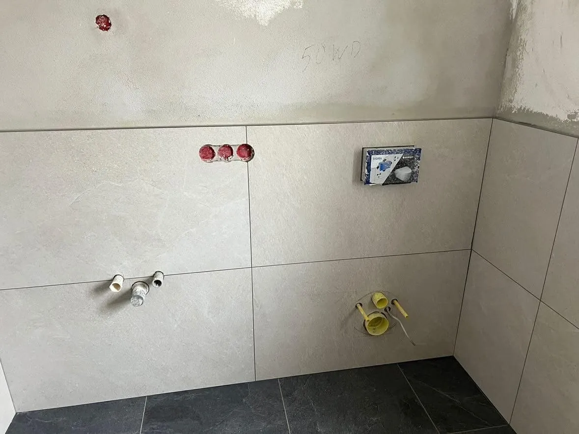 Badwand mit beigen Großformatfliesen und Anschlüssen für die Armatur