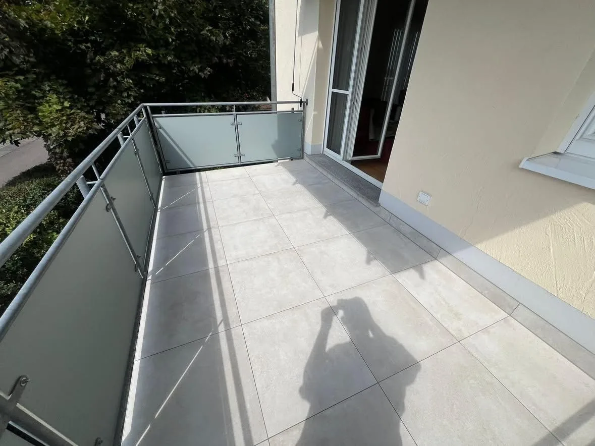 Terrasse mit grauen Großformat-Feinsteinzeugfliesen und Glasgeländer
